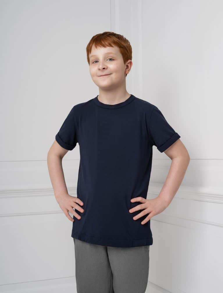 An autistic boy stands with hands on hips, wearing a dark blue, sensory friendly T-shirt that has popit fidgets sewn into the hem called the Fidget-T.
