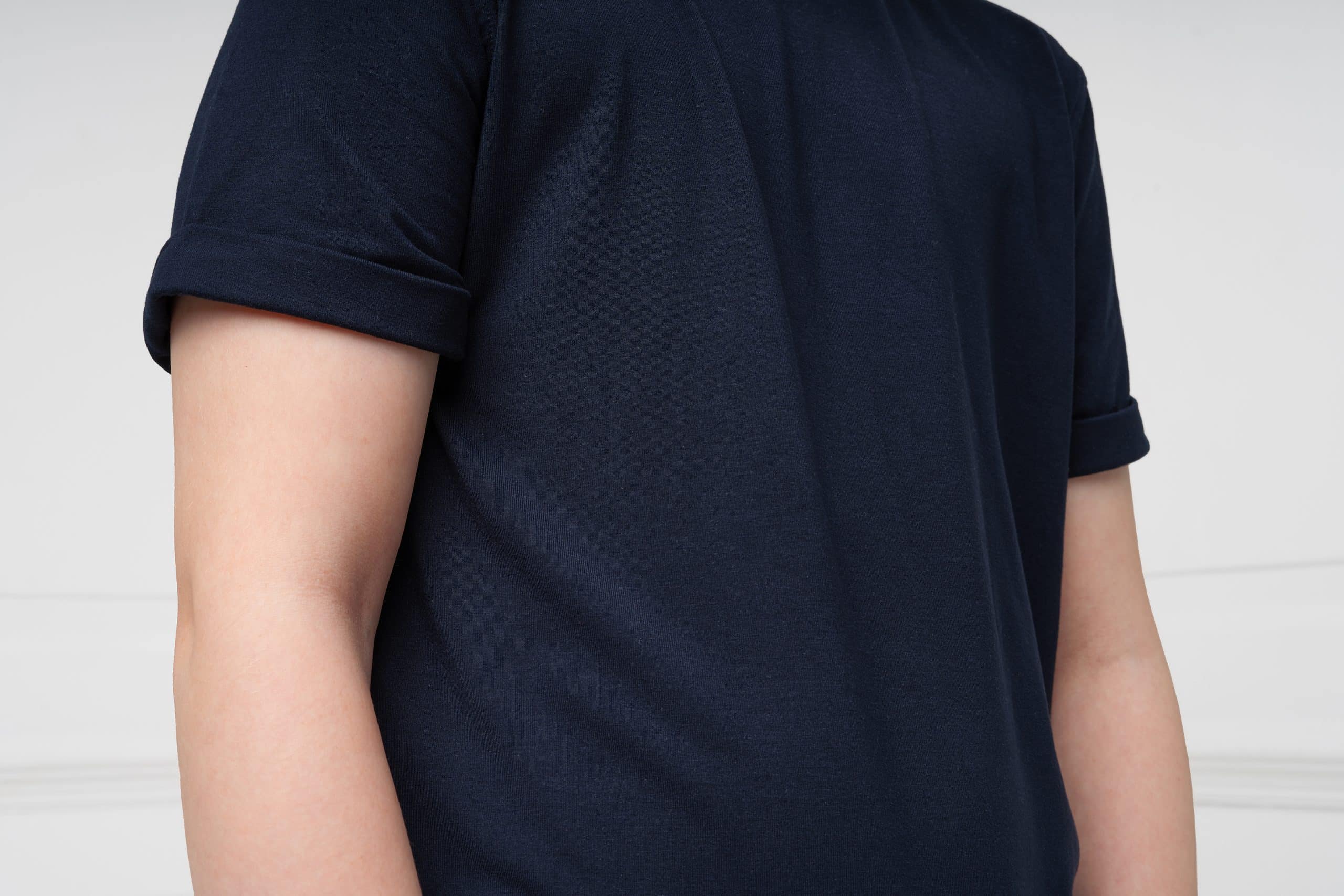 A close up of the sleeves and top of the body of a young autistic boy, wearing a dark blue Fidget-T T-shirt. the sleeves can be seen to have rolled back cuffs on them, to protect the wearer from any seams.