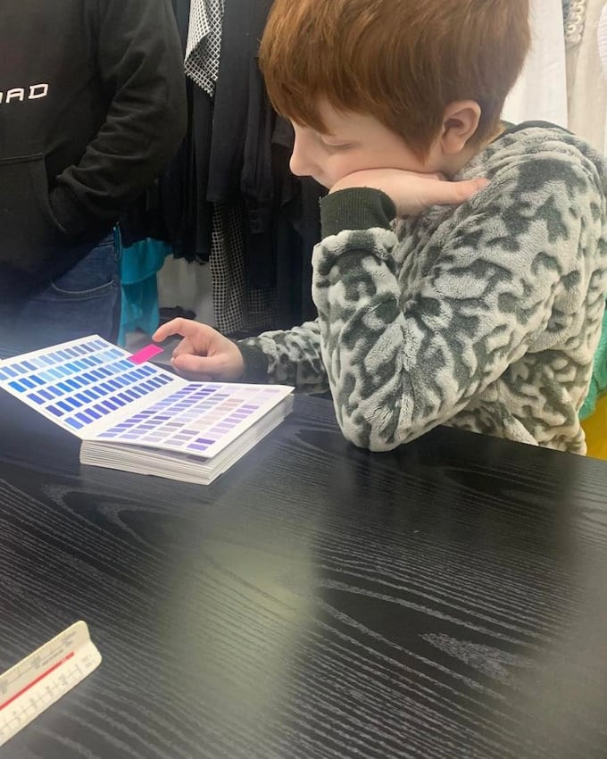 A young autistic boy with ginger hair chooses colour selections from a book, for the prototype model of his sensory clothing range