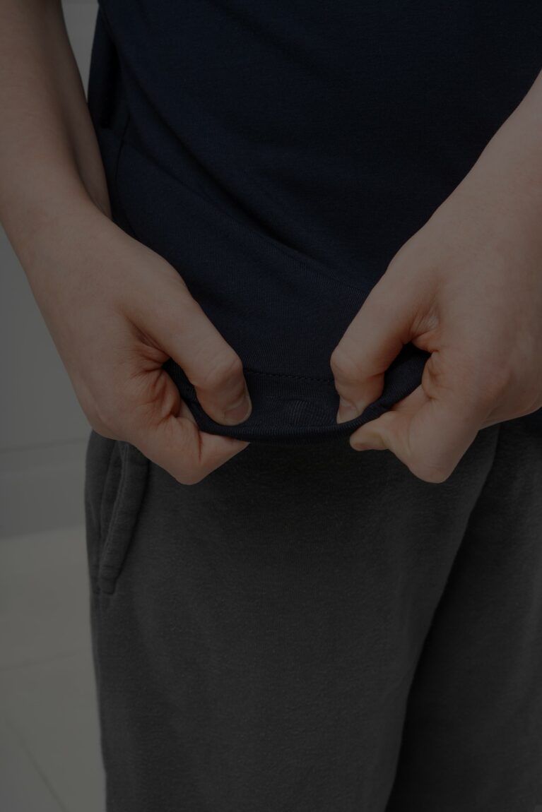 A close up of a neurodiverse boy with autistim playing with the hidden popit feature in the hem of the Fidget-t. 3 popits can be seen, with 2 being pressed and 1 in the middle unpressed.